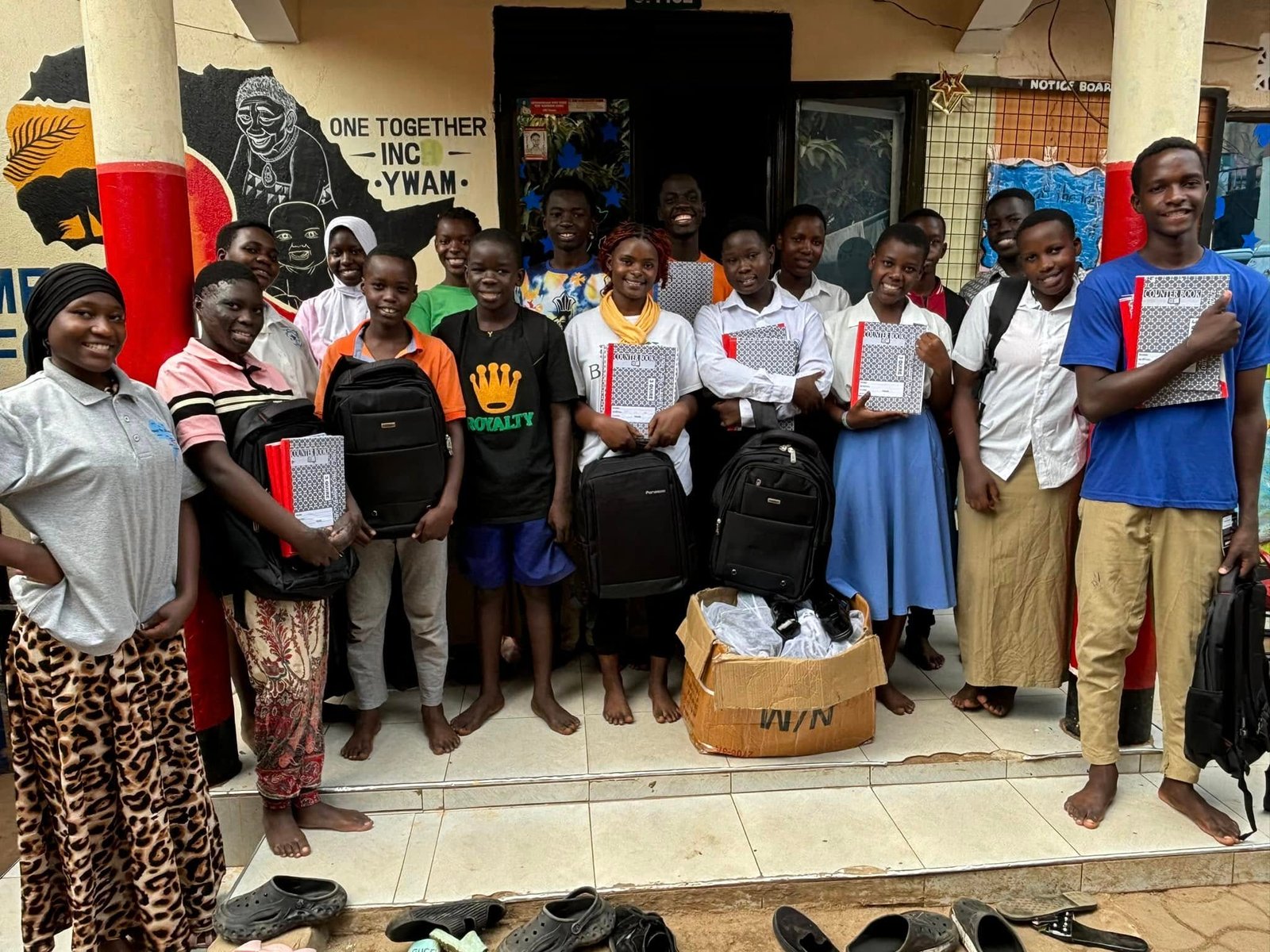 A group of Mercy School students stand on the office steps holding new backpacks and exercise books