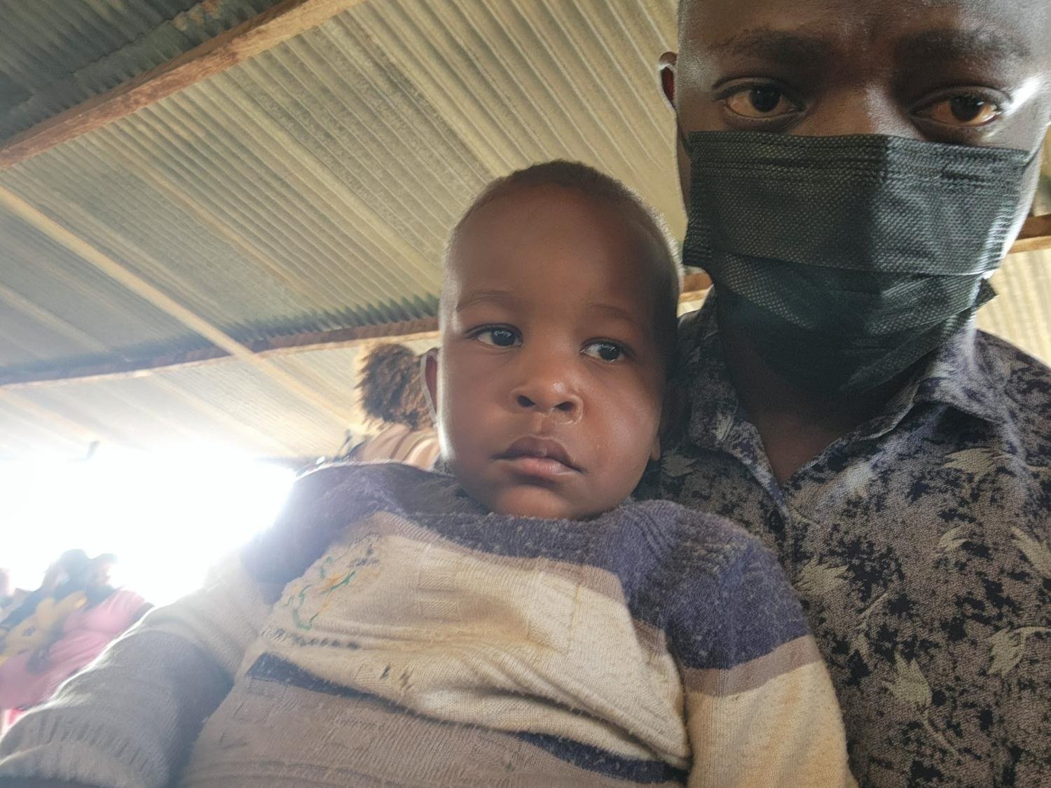 A staff member holds a toddler on the way to medical care in Kampala